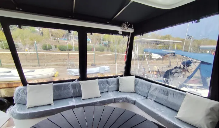 Şeffaf pencereli koyu renk kapama ile çevrilmiş flybridge; içinde yeni gri minderler ve beyaz kırlentler