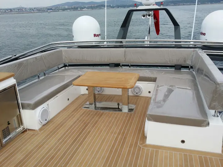 Yeni dikilmiş gri minderleriyle flybridge oturma alanı, ortada teak masa